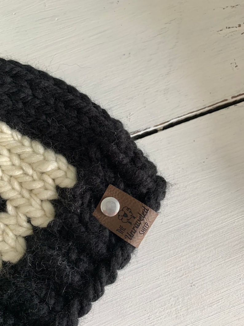 May include: Black and white knitted hat with a brown leather tag that says "The Unraveled Sheep".