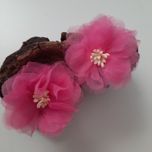 Op de afbeelding: Twee roze bloemen van stof met witte centra. De bloemen zijn gemaakt van een doorschijnend materiaal en hebben een delicate, gerimpelde uitstraling.