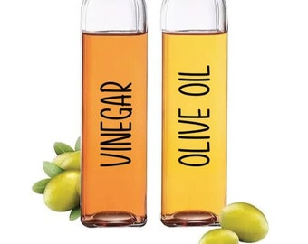 Puede incluir: Dos botellas de vidrio transparente con boquillas de vertido negras y etiquetas. La botella de la izquierda está etiquetada como "Vinagre" y contiene un líquido amarillo. La botella de la derecha está etiquetada como "Aceite de oliva" y contiene un líquido amarillo claro.