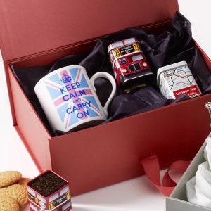 May include: A red gift box with a black and white patterned lining. The box contains a white mug with a blue and pink Union Jack flag and the text "Keep Calm and Carry On". There are also two small tin boxes, one with a red double-decker bus and the text "English Breakfast Tea" and the other with a map of London and the text "London Tea".