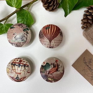 Op de afbeelding: Vier ronde houten dozen met vintage ontwerpen. Elke doos heeft een ander beeld, waaronder een luchtballon, een zwaan, een kraanvogel en een andere luchtballon. De dozen zijn op een wit oppervlak gerangschikt.