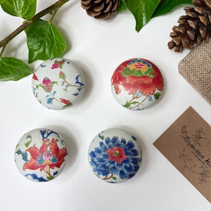 May include: Four round ceramic knobs with floral patterns. The knobs are white with red, blue, and green floral designs. The knobs are arranged in a square pattern on a white surface.
