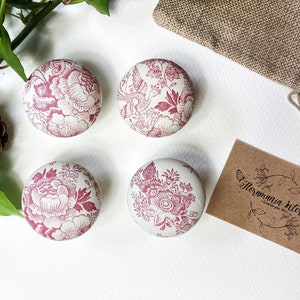 Może przedstawiać: Cztery okrągłe drewniane gałki z białym tłem i różowym wzorem kwiatowym. Gałki są ułożone w kwadrat na białym tle. Mała brązowa karta z tekstem "Flormania Interiors" znajduje się w prawym dolnym rogu obrazu.