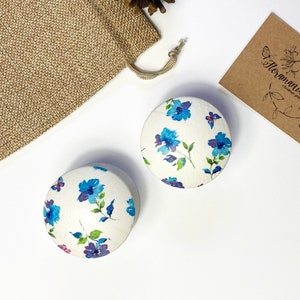 May include: Two round wooden boxes with a white background and a blue floral pattern. The boxes are on a white surface.