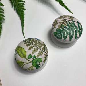 May include: Two round, white ceramic knobs with a green and white fern pattern.