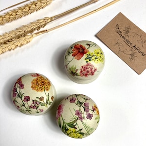 Könnte beinhalten: Drei runde Holzkisten mit Blumendesigns. Die Kisten sind mit verschiedenen Blumen verziert, darunter rote, rosa, gelbe und grüne. Die Kisten sind alle unterschiedlich groß und in einer Reihe angeordnet.