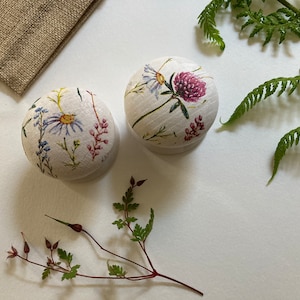 May include: Two round wooden boxes with floral designs. The boxes are white with pink, green, and yellow flowers. The boxes are on a white surface.