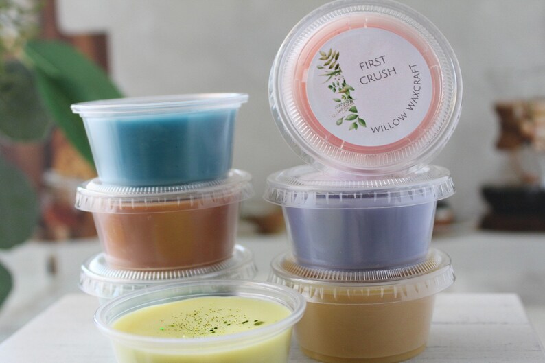 May include: Six small clear plastic containers filled with different colored wax melts. The top container has a pink wax melt with a label that reads "First Crush Willow Waxcraft".