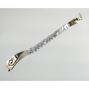 May include: A silver and gold watch band with a unique design. The band is made of metal links and has a decorative pattern.