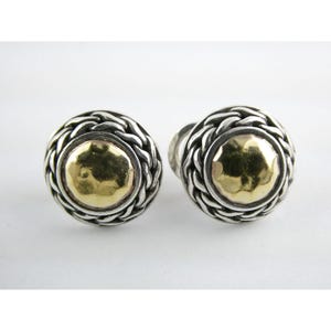 Pode incluir: Um par de brincos de botão prateados com um design de borda trançada. Cada brinco apresenta um centro dourado martelado. Os brincos são redondos e têm fecho de pino.