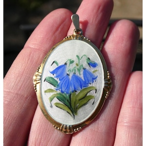 Peut inclure: Pendentif ovale en argent avec un motif floral en émail bleu et vert. Le pendentif est entouré d'une bordure dorée avec de petites perles.