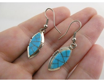 May include: A pair of silver-toned earrings with a turquoise inlay. The earrings have a teardrop shape with a geometric design in the center. The earrings are displayed against a neutral background.