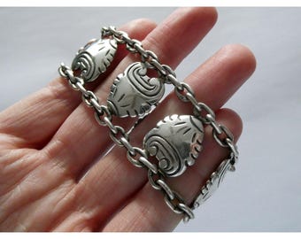 May include: A silver bracelet with a chain design, featuring decorative, leaf-shaped links. The links are connected by a chain and have etched details. The bracelet has a polished finish, giving it a vintage or antique appearance.