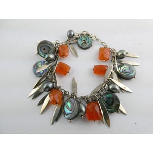 May include: A silver charm bracelet featuring a variety of decorative elements. The bracelet includes orange-colored, rectangular beads, iridescent abalone shell charms, gray pearl beads, and silver leaf-shaped charms. The bracelet is designed with a chain link.