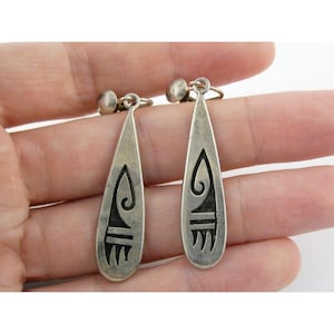 May include: A pair of silver-toned drop earrings. Each earring has a teardrop shape with a decorative black design. The earrings have a post and clip-on style.