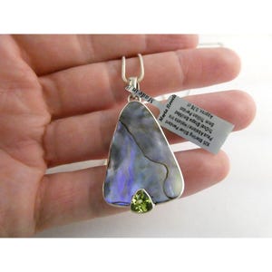 May include: A sterling silver pendant with a triangular paua abalone pendant and a 6mm trillion peridot. The pendant has a silver chain. The tag reads "Marta Howell" and "Made in B".