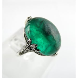 Op de afbeelding: Een zilveren ring met een grote, ovale, groene edelsteen.