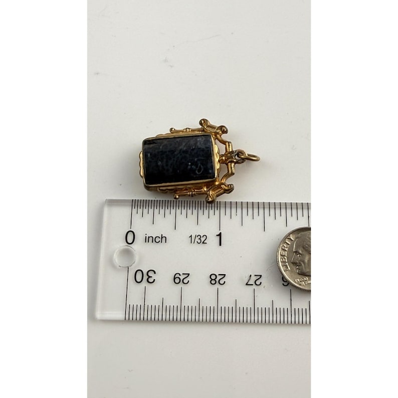 May include: A small, rectangular pendant with a dark blue stone set in a gold-coloured metal frame. The pendant is approximately 1.9 cm long. A ruler and a coin are next to the pendant.