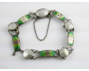 Puede incluir: Pulsera plateada con elementos ovalados y redondos. La pulsera tiene eslabones ovalados con diseños de esmalte verde y morado y detalles redondos blancos perlados. Una delicada cadena asegura la pulsera. Aproximadamente 18 cm de largo.