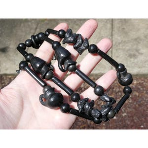 Puede incluir: Collar de cuentas negras con colgantes tallados en negro. Los colgantes tienen forma de animales pequeños y una tetera.