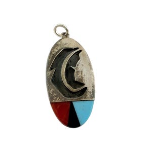 May include: An oval-shaped silver pendant featuring a cutout crescent moon design at the top. The lower section is inlaid with three distinct triangular segments of red, black, and light blue stone, finished with a small silver jump ring at the top.