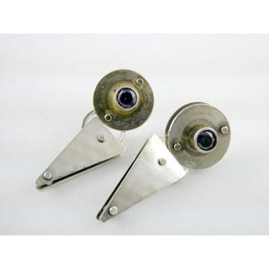 Peut inclure: Une paire de boucles d'oreilles en argent au design géométrique. Chaque boucle d'oreille présente un dessus circulaire avec une pierre précieuse bleu foncé et un pendentif triangulaire. Les boucles d'oreilles sont en métal et ont un style moderne et minimaliste.