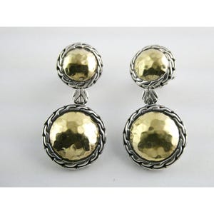 Pode incluir: Um par de brincos de prata e ouro. Cada brinco apresenta um disco dourado martelado rodeado por uma borda prateada em forma de corda. Os brincos são pendurados, com um disco dourado menor no topo.