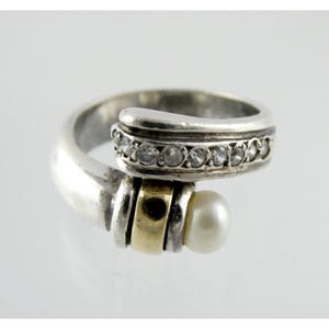 May include: A silver ring featuring a pearl and a row of clear stones. The ring has a gold band.