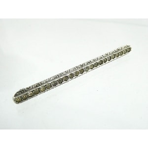 May include: A silver bar brooch with a row of clear rhinestones set in a decorative pattern.