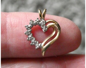 May include: A gold-toned heart pendant with a cluster of small, sparkling stones along one side. The pendant has a curved, open design and a small loop for a chain. The jewelry is displayed against a blurred background.