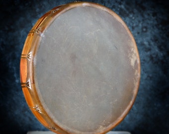 May include: A brown leather drum with a wooden frame and decorative metal accents. The drum is sitting on a wooden surface.