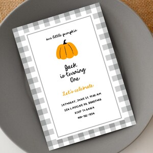Pode incluir: Um convite de aniversário com uma borda xadrez cinza e branca. O texto diz "our little pumpkin" e "Jack is turning One". Uma ilustração de abóbora laranja está no topo. O convite inclui a data, hora e local.