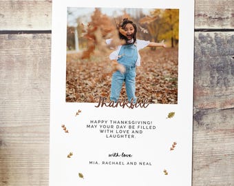 May include: A Thanksgiving card with a photo of a child in a blue overall jumping in a pile of autumn leaves. The card reads "Thankful! Happy Thanksgiving! May your day be filled with love and laughter. With love, Mia, Rachael and Neal."