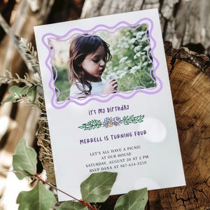 May include: A birthday invitation featuring a photo of a young child within a wavy lavender frame. The text "it's my birthday" is above the photo, and "Merrell is turning four" is below. Additional text includes picnic details and RSVP information.