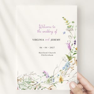 Op de afbeelding: Een huwelijksvoltrekking met een bloemmotief met verschillende bloemen in tinten paars, blauw, geel en roze. De tekst luidt "Welkom op de bruiloft van VIRGINIA en JEREMY 06.04.2027 Hartiford Church Cheltenham."