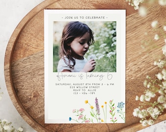 May include: A white invitation card with a photo of a young girl blowing on a dandelion. The text on the card reads "Join us to celebrate - Amani is turning 6. Saturday, August 8th from 3 - 6 PM. 525 Willow Street. RSVP to Allie. 123-456-789". The card is decorated with a watercolor illustration of wildflowers.