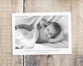 May include: Black and white photo of a baby boy named Hayden Jameson. The baby is lying on a white blanket and smiling. The photo is on a white card with the text "Thank you for your thoughtful gift and well wishes. Love, Hailey & Nick."