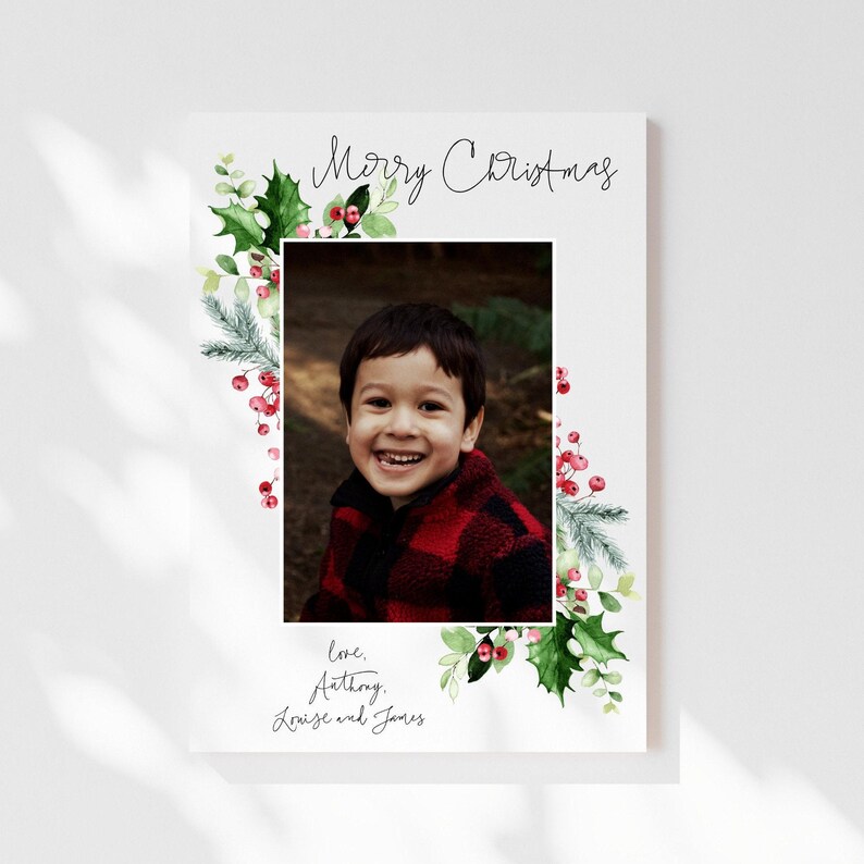 May include: A Christmas card with a watercolor border of holly and berries. A photo of a young boy smiling is in the center of the card. The text "Merry Christmas" is at the top of the card and "love, Anthony, Louise and James" is at the bottom.