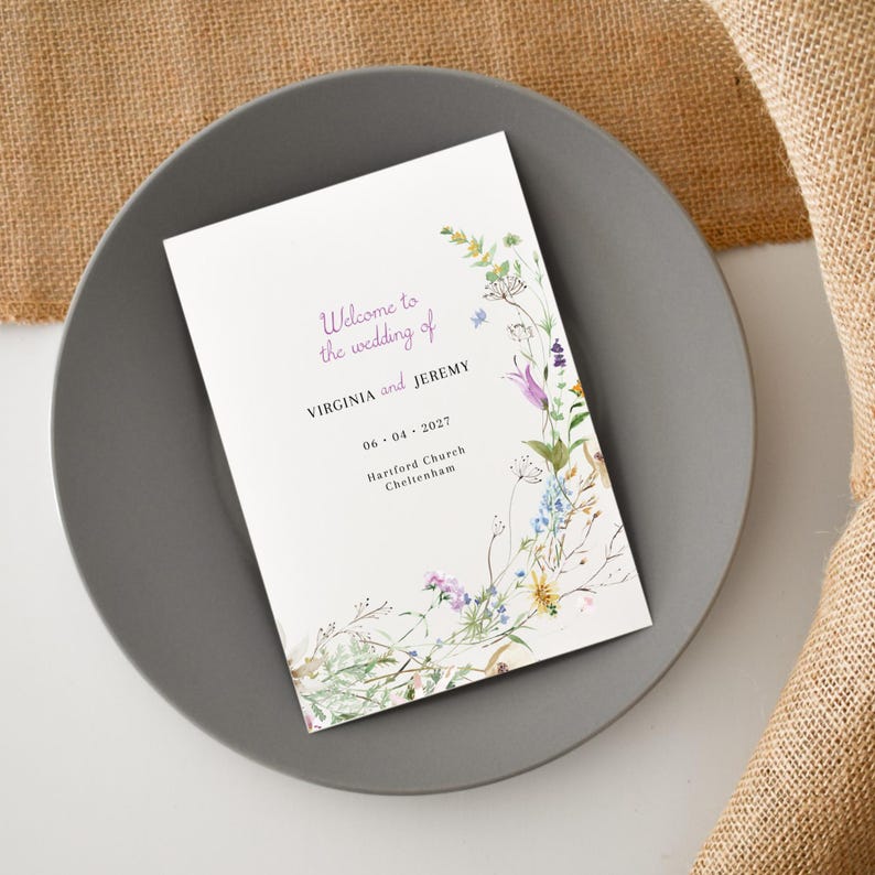 May include: A white wedding program with a floral design featuring a variety of wildflowers in shades of purple, blue, yellow, and green. The text reads "Welcome to the wedding of VIRGINIA and JEREMY 06.04.2027 Harlford Church Cheltenham."