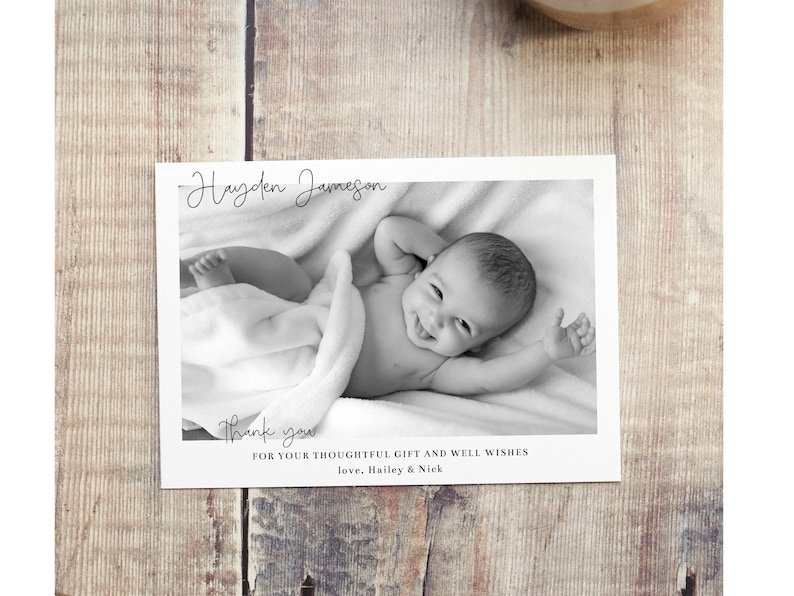 May include: Black and white photo of a baby boy named Hayden Jameson. The baby is lying on a white blanket and smiling. The photo is on a white card with the text "Thank you for your thoughtful gift and well wishes. Love, Hailey & Nick."