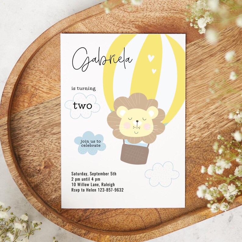 May include: A birthday invitation featuring a yellow hot air balloon with a lion illustration. The invitation includes the name "Gabriela", the words "is turning two", and event details. The design is set on a white background.