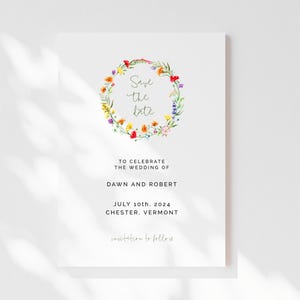 May include: Save the date wedding announcement with a floral wreath in shades of red, yellow, orange, purple, and green. The text reads "Save the date" and includes the wedding date of July 10th, 2024 and the location Chester, Vermont.