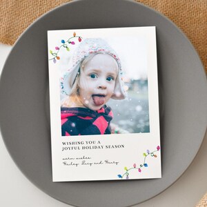 Puede incluir: Una tarjeta de felicitaci&oacute;n navide&ntilde;a con una foto de un ni&ntilde;o sacando la lengua, con un gorro de invierno y una parte superior estampada en rojo y negro. La tarjeta incluye el texto "Wishing you a joyful holiday season" y los nombres "Hailey, Lucy and Henry."