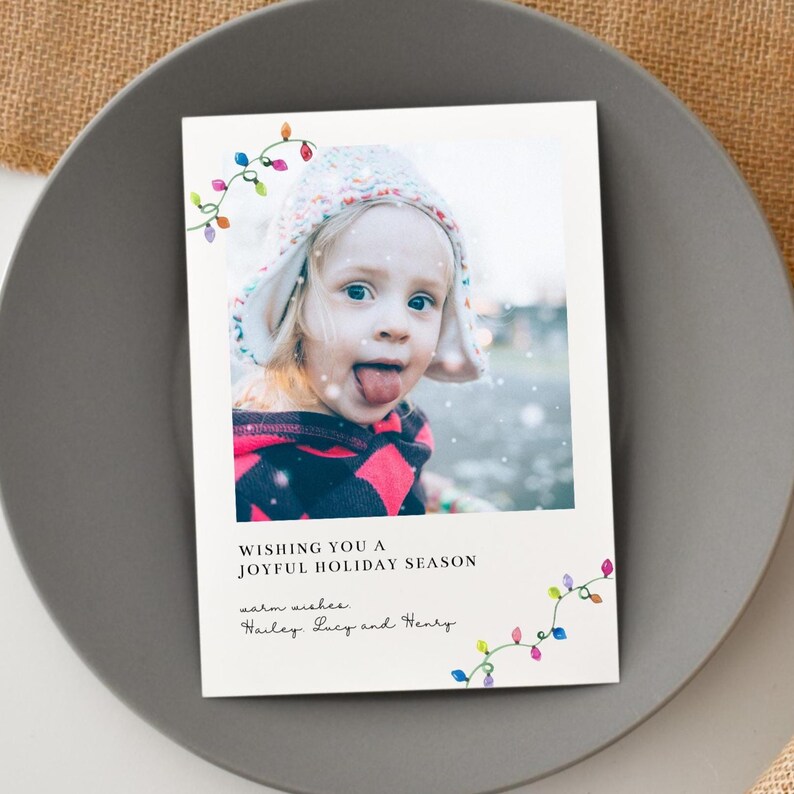 Puede incluir: Una tarjeta de felicitaci&oacute;n navide&ntilde;a con una foto de un ni&ntilde;o sacando la lengua, con un gorro de invierno y una parte superior estampada en rojo y negro. La tarjeta incluye el texto "Wishing you a joyful holiday season" y los nombres "Hailey, Lucy and Henry."