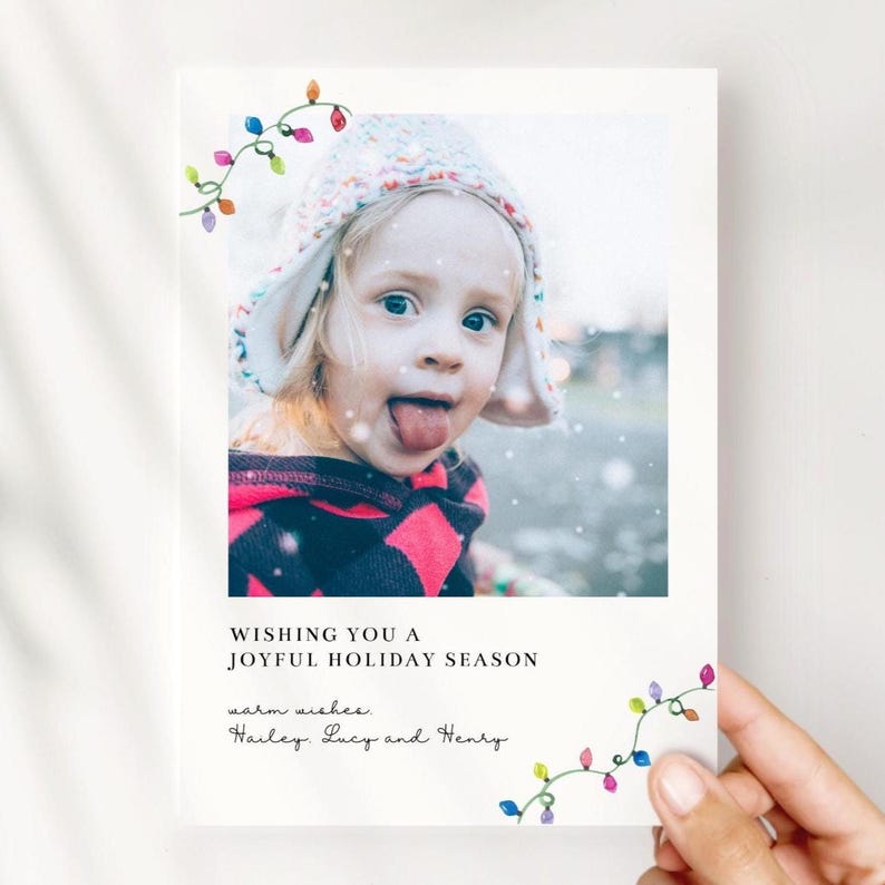 Puede incluir: Tarjeta de felicitaci&oacute;n navide&ntilde;a con una foto de un ni&ntilde;o sacando la lengua, con un gorro de punto y una parte superior rosa y negra. La tarjeta dice "WISHING YOU A JOYFUL HOLIDAY SEASON" y "warm wishes, Hailey, Lucy and Henry."