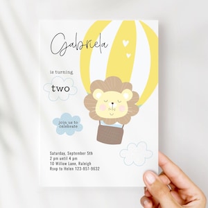 May include: A birthday invitation featuring a lion in a hot air balloon. The invitation has the name "Gabriela" in script, the words "is turning two", and event details. The design includes yellow, brown, and blue elements.