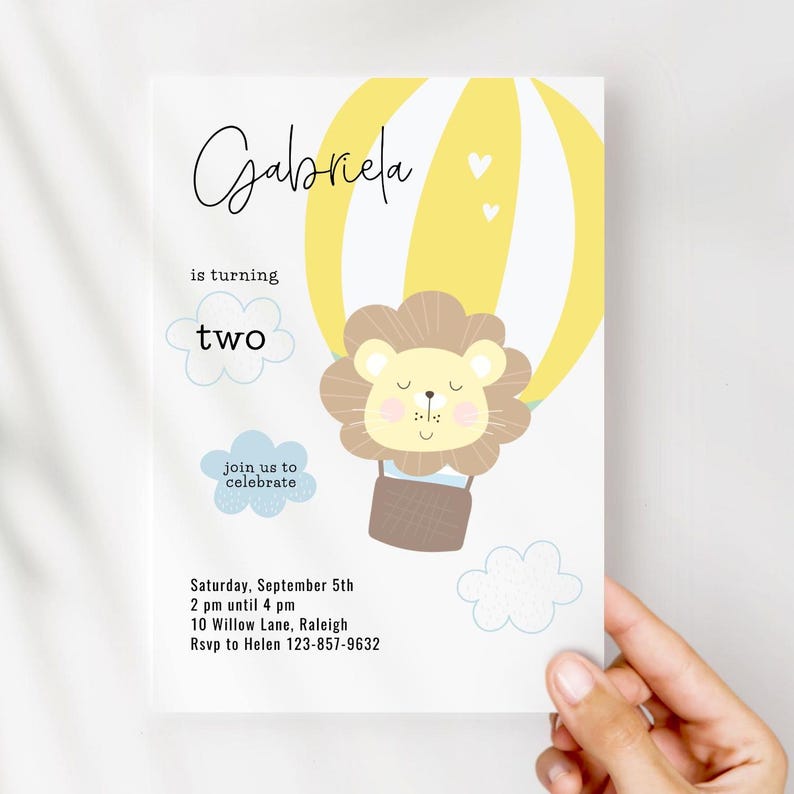 May include: A birthday invitation featuring a lion in a hot air balloon. The invitation has the name "Gabriela" in script, the words "is turning two", and event details. The design includes yellow, brown, and blue elements.