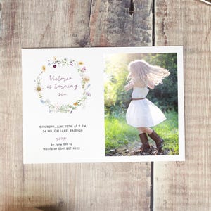 May include: A floral wreath with the text "Victoria is turning six" in purple script. A photo of a girl in a white dress and brown boots is on the right side of the card. The text below the wreath reads "Saturday, June 10th, at 2 PM 56 Willow Lane, Raleigh RSVP by June 5th to Nicola at 0541 857 9632"