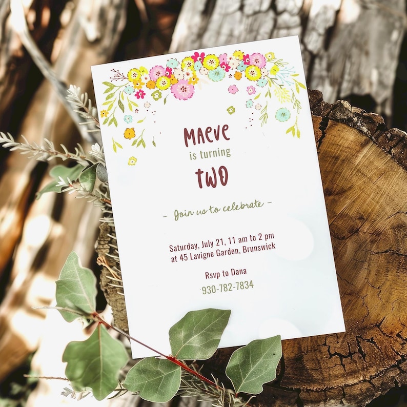 May include: A floral-themed birthday invitation for a child named Maeve turning two. The invitation features a colorful floral garland with pink, yellow, and green flowers. The text on the invitation reads "Maeve is turning two" and includes details about the party, including the date, time, location, and RSVP information.