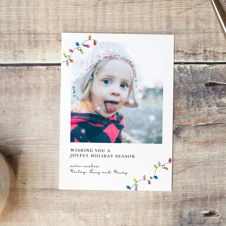 Puede incluir: Tarjeta de felicitaci&oacute;n navide&ntilde;a con la foto de un ni&ntilde;o sacando la lengua, con un dise&ntilde;o de luces de colores. La tarjeta incluye el texto "Wishing you a joyful holiday season" y los mejores deseos de Hailey, Lucy y Henry.